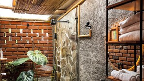 A bathroom with a stone wall, a wooden ceiling, a toilet, a sink, and a shower. - Artisanal Amazonian Suite, A Natural Refuge in Puyo (Puyo)