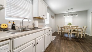 A kitchen with white cabinets, a sink, and a dining area with a table and chairs. - Cozy & Quiet - CENTRAL Location - Master’s Retreat! (Augusta)