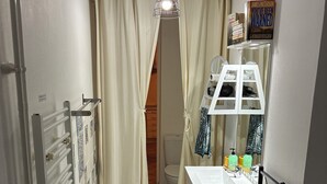 Een kleine badkamer met een witte radiator, een handdoekhouder, een plank met toiletartikelen en een boek aan de muur.