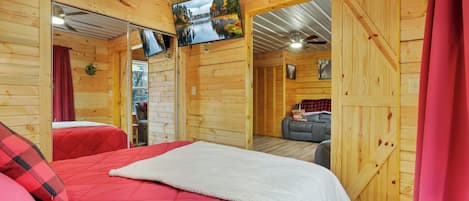 A cozy cabin-style room with a large bed, a television mounted on the wall, and a wooden door leading to another room.