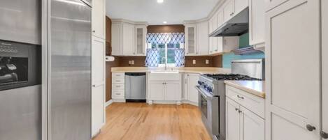 A modern kitchen with white cabinets, stainless steel appliances, and a wooden floor.
