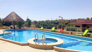 Ein Pool mit Whirlpool, umgeben von Liegestühlen und einer überdachten Struktur mit einem Reetdach.