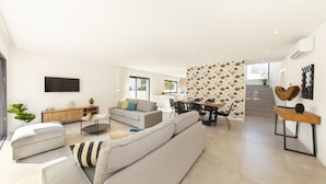 A modern living room with a sofa, a dining table, and a staircase leading to an upper floor. - Villa with heatable pool near the Marina (Quarteira)