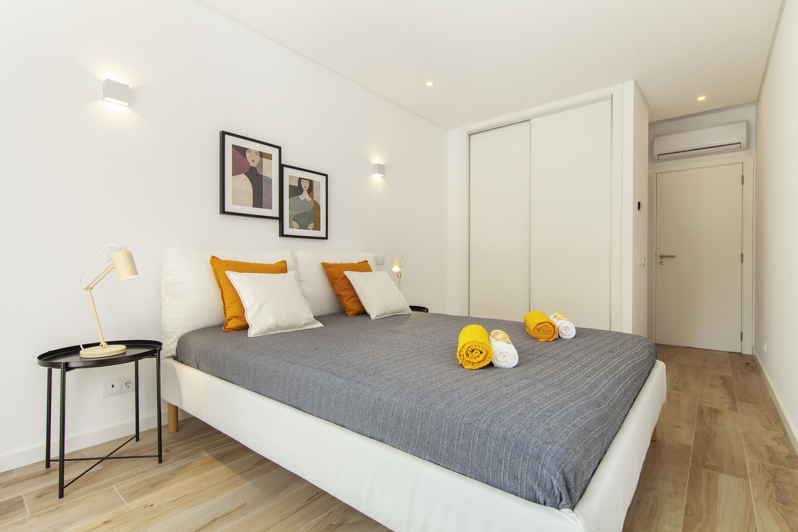 A modern bedroom with a large bed, a bedside table, a wall-mounted light, and a door.