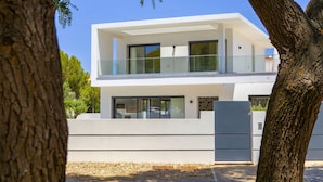 A modern two-story building with a balcony, large windows, and a stone base. - Villa with heatable pool near the Marina (Quarteira)