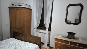 A bedroom with a wooden wardrobe, a bed with a floral bedspread, a dresser with drawers, a mirror, and a window with sheer curtains. - CASA FIVIZZANO A vacation home in Tuscan style. Pet friendly (Fivizzano)