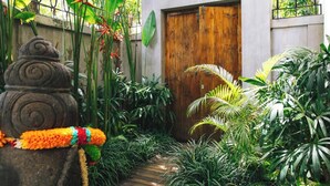 Ein tropischer Garten mit einer Holztür, einer Steinstatue und unterschiedlicher Bepflanzung.