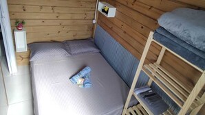 Una stanza piccola e accogliente, con un muro in legno, un letto con materasso blu, un letto a castello in legno e un comodino bianco con una lampada.