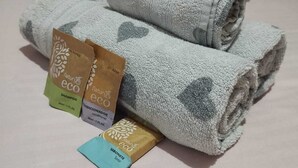 Un letto rifatto con asciugamani piegati e tre confezioni di prodotti ecologici.
