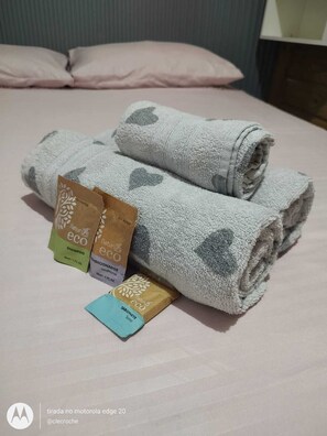 A neatly made bed with folded towels and three eco-friendly product packages. - 2-bedroom house 850m from the beach, north of the island (Florianópolis)