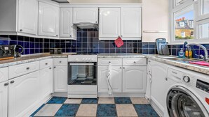 Una cocina con armarios blancos, horno empotrado, lavadora y ventana con vista a una casa.