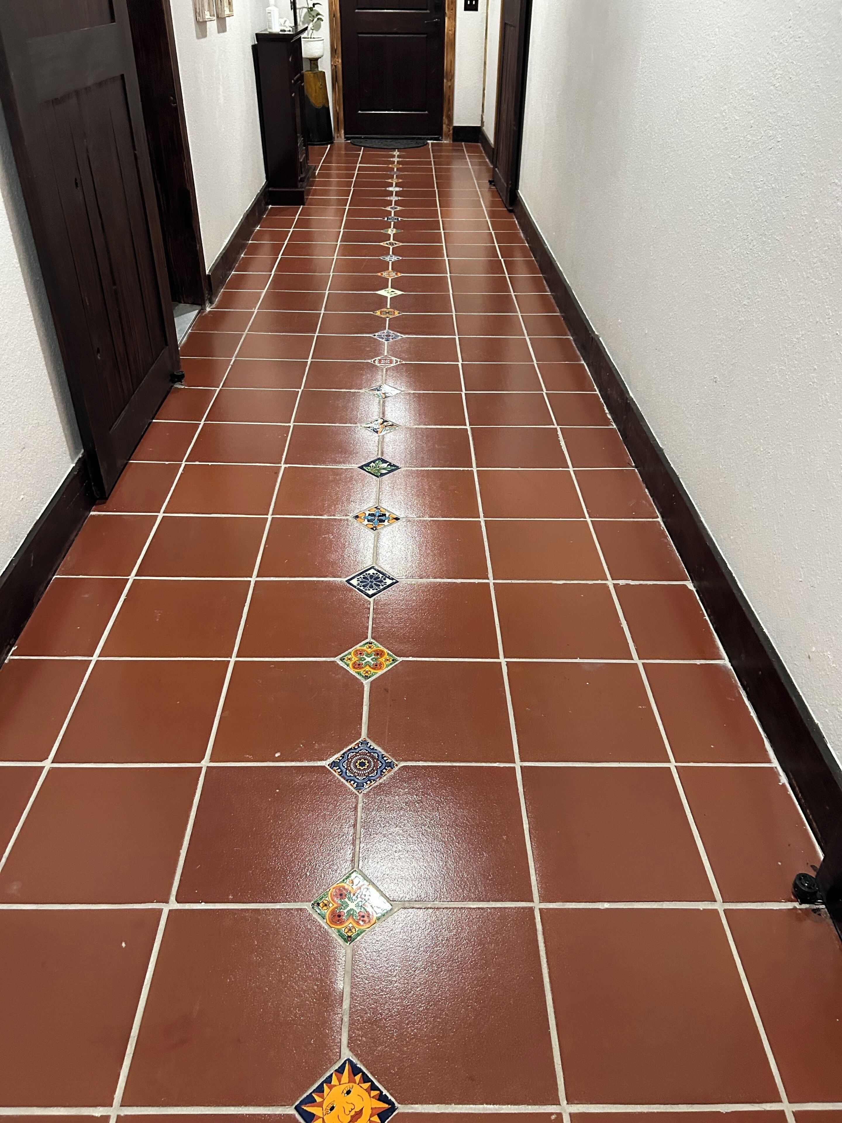 A hallway with brown tiled flooring and decorative tiles in a pattern.