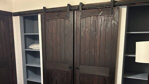 Een kamer met houten vloer, een bed met een beddegoed met patroon, een kapstok en een grote schuifdeurkast met planken.