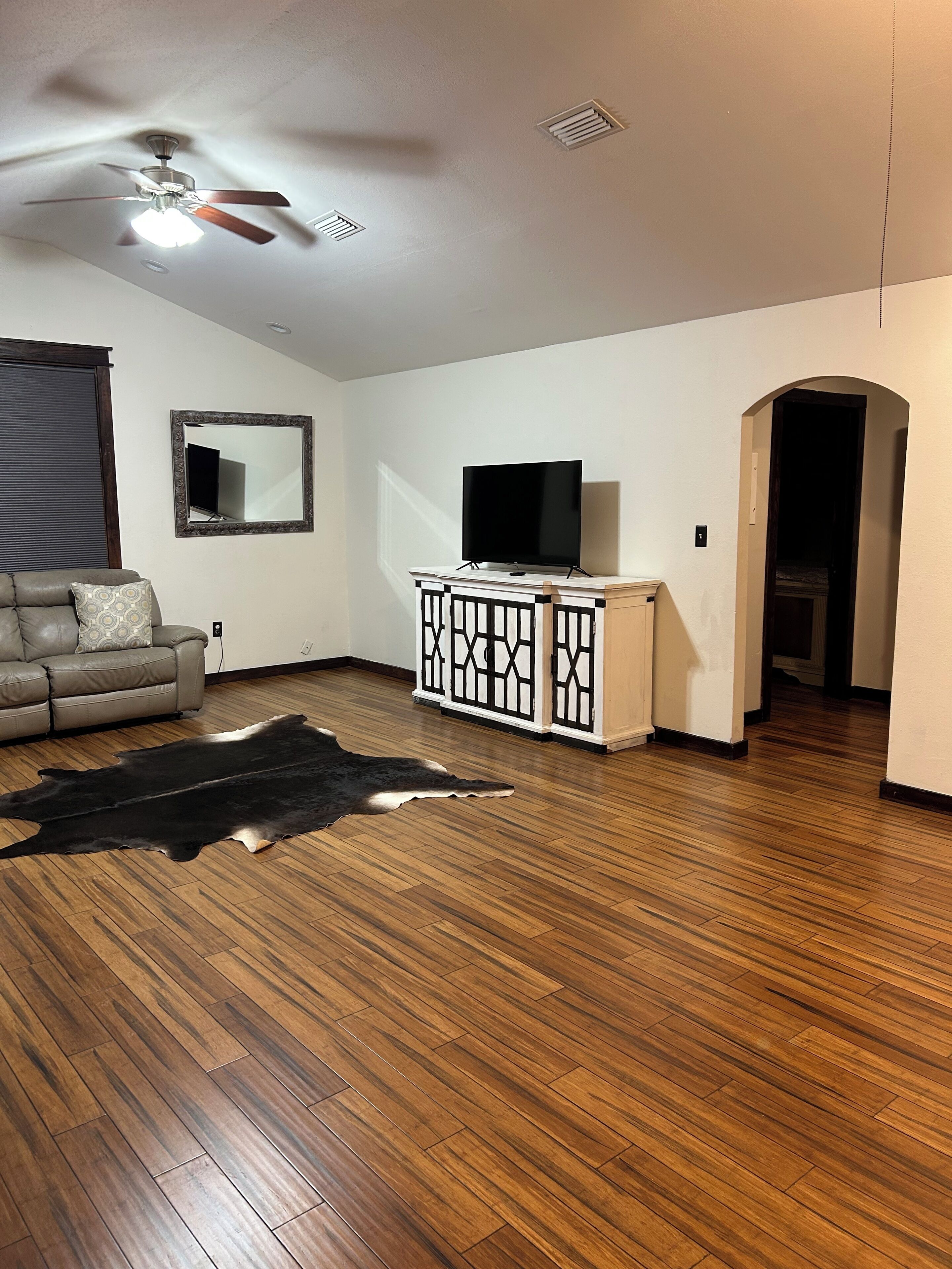 A living room with a sofa, a television on a cabinet, a ceiling fan, and a wooden floor.