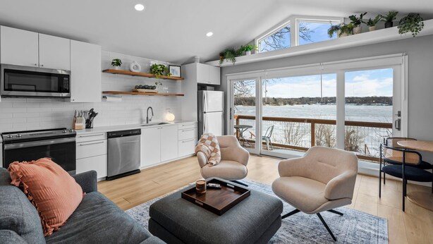A modern kitchen with white cabinets, a microwave, and a refrigerator. There is a dining area with a table and chairs, and a large window overlooking a scenic view. - Cozy Lake Retreat w/ Private Dock in Arden Hills! (Arden Hills)