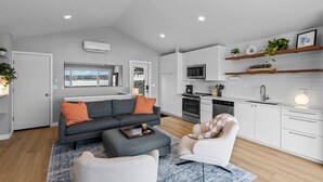 A modern living room with a grey sofa, a white armchair, and a coffee table. There is a kitchen with white cabinets, a microwave, and a sink. - Cozy Lake Retreat w/ Private Dock in Arden Hills! (Arden Hills)