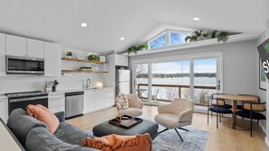 A modern kitchen with white cabinets, a microwave, and a dishwasher. There is a dining area with a table and chairs, and a sofa with cushions. - Cozy Lake Retreat w/ Private Dock in Arden Hills! (Arden Hills)
