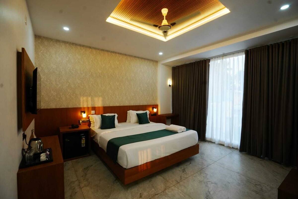 A modern hotel room with a large bed, a flat-screen TV, a bedside table with a lamp, and a ceiling fan.