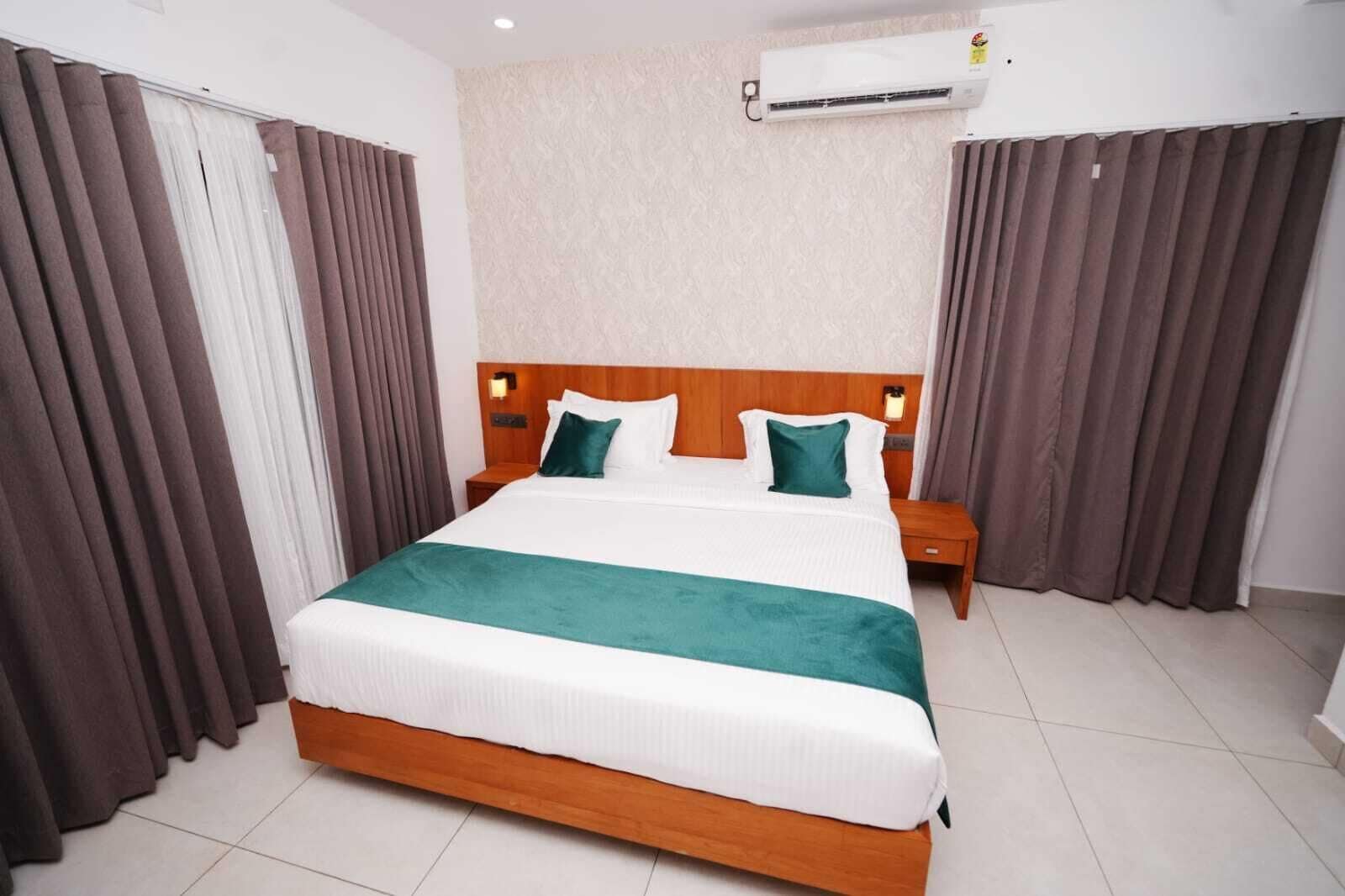 Una habitación de hotel con una cama grande, dos mesitas de noche, un aire acondicionado y cortinas.