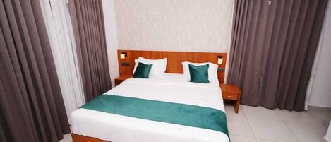 Una habitación de hotel con una cama grande, dos mesitas de noche, un aire acondicionado y cortinas.