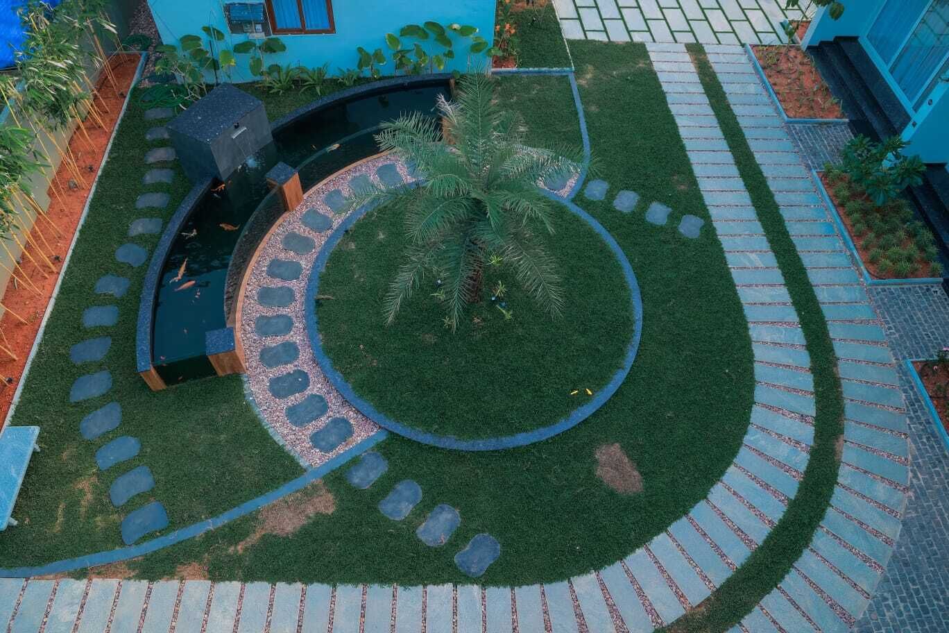 A circular garden with a central palm tree, surrounded by a stone path and grass.