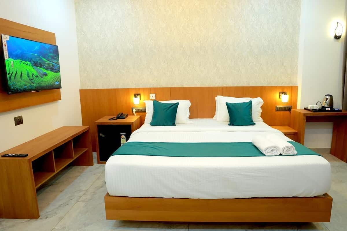 A hotel room with a large bed, two bedside tables with lamps, a TV mounted on the wall, and a wooden bench.