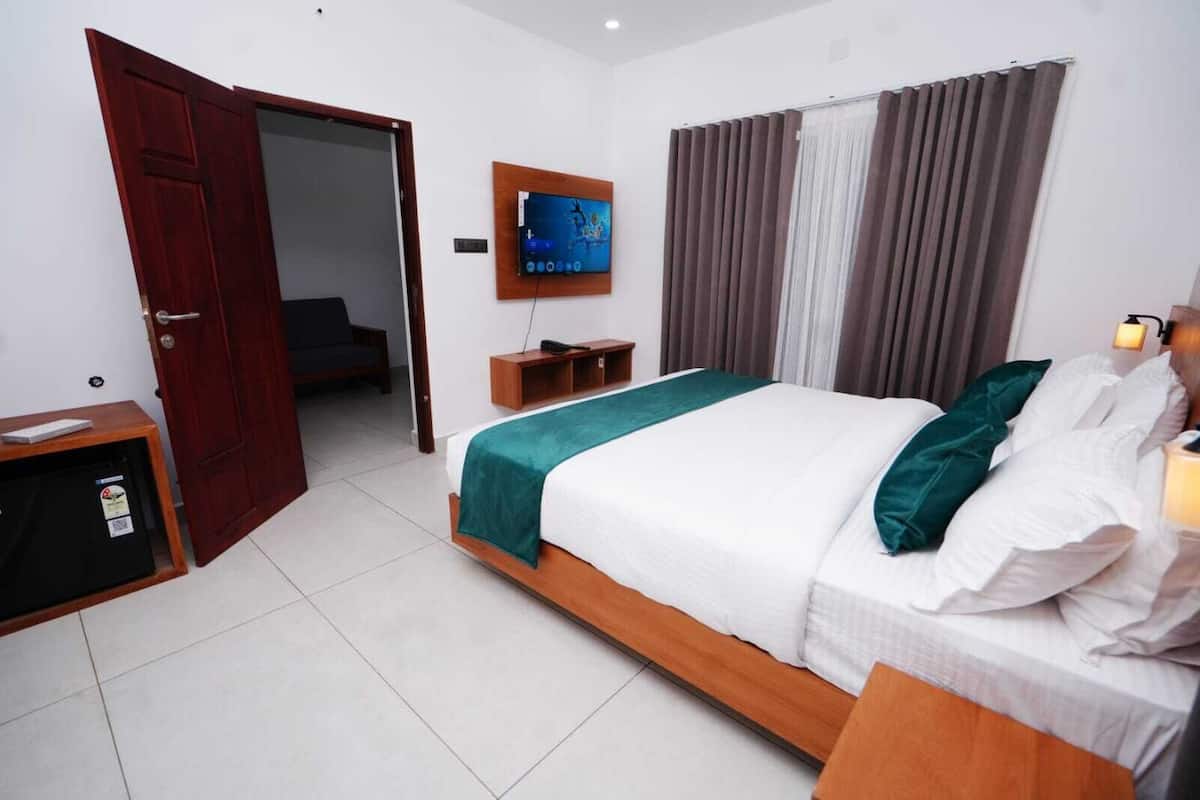 A hotel room with a bed, a TV mounted on the wall, a desk with a computer, and a door leading to another room.