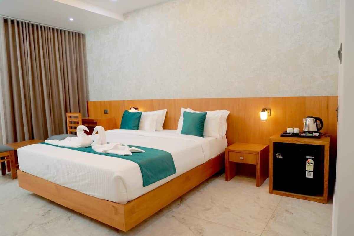 A hotel room with a large bed, wooden headboard, two bedside tables, a nightstand, a small cabinet, and a curtain.
