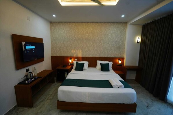 A hotel room with a large bed, two bedside tables, a flat-screen TV, a wall-mounted lamp, and a window with curtains.