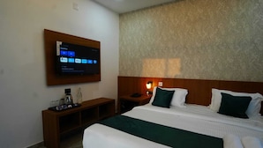 A hotel room with a bed, a TV mounted on the wall, a bedside table with a lamp, and a wooden headboard. - Palm Wave Beach Resort (Kochi)