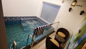 A modern indoor swimming pool with a tiled edge, a glass door, and a lounge area with a chair and a small table. - Palm Wave Beach Resort (Kochi)