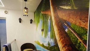 A lobby with a large mural of a tropical landscape, a black wicker chair, a glass elevator, and a wall-mounted light fixture. - Palm Wave Beach Resort (Kochi)