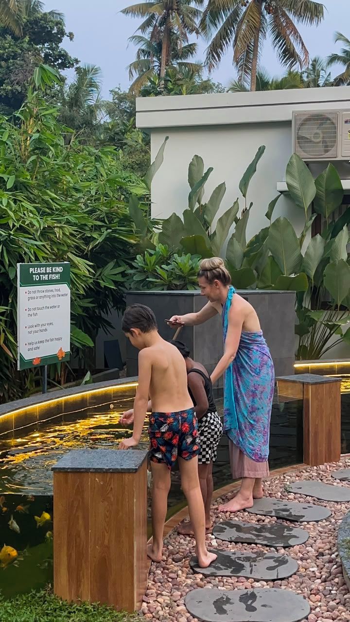 A pond with stepping stones, a sign advising to be kind to the fish, and a person assisting a child.