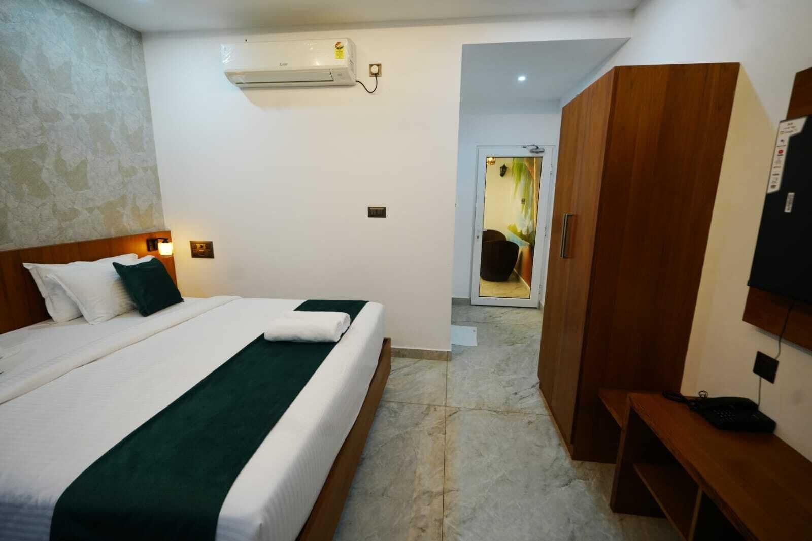 A hotel room with a bed, a wardrobe, a desk, and an air conditioning unit.