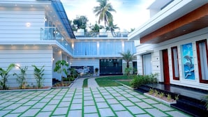 A modern hotel with a spacious courtyard, a covered outdoor area, and a view of palm trees. - Palm Wave Beach Resort (Kochi)