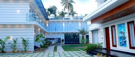 A modern hotel with a spacious courtyard, a covered outdoor area, and a view of palm trees.