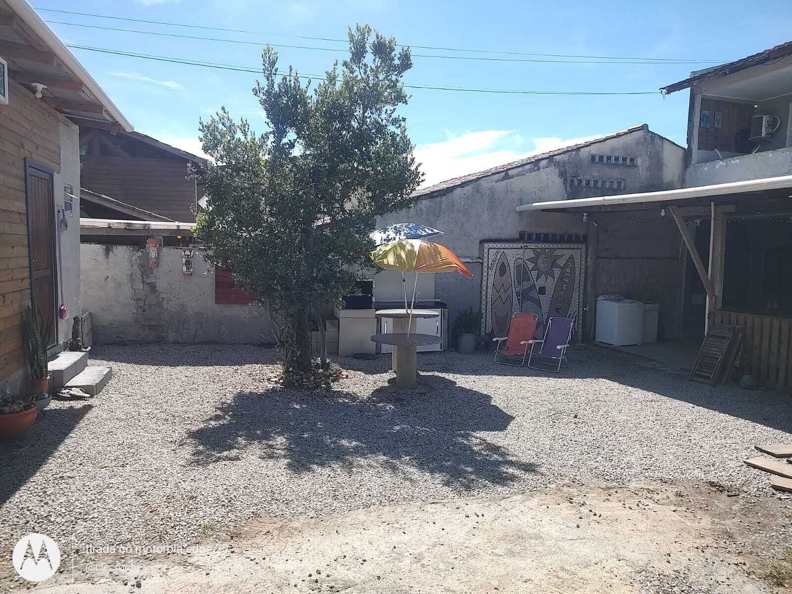 A gravel courtyard with a tree, a small table, and a chair under a sun umbrella.