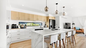 Uma cozinha moderna com armários brancos, uma ilha de mármore e iluminação pendente.