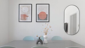 Ein stilvolles Esszimmer mit grauem Tisch, zwei gerahmten Kunstwerken, einer Vase mit Trockenpflanzen und einem runden Spiegel an der Wand.