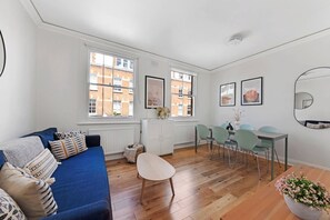 A modern living room with a blue sofa, a dining table with chairs, and a large window with a view of buildings. - Bell Street NW1, Edgware Rd, Marylebone (London)