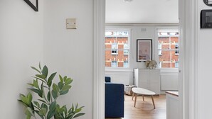 Ein modernes Apartment mit Holzboden, einem blauen Sofa, einem weißen Tisch und Blick auf rote Backsteingebäude durch große Fenster.
