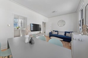 A modern living room with a blue sofa, a flat-screen TV, and a dining area with a table and chairs. - Bell Street NW1, Edgware Rd, Marylebone (London)