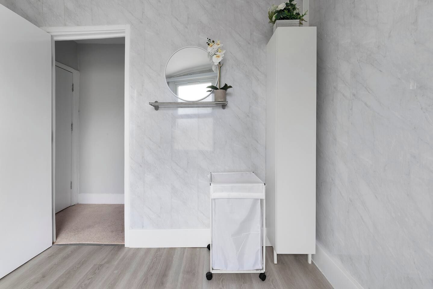 Een badkamer met een wit aanrecht, een ronde spiegel en een potplant.