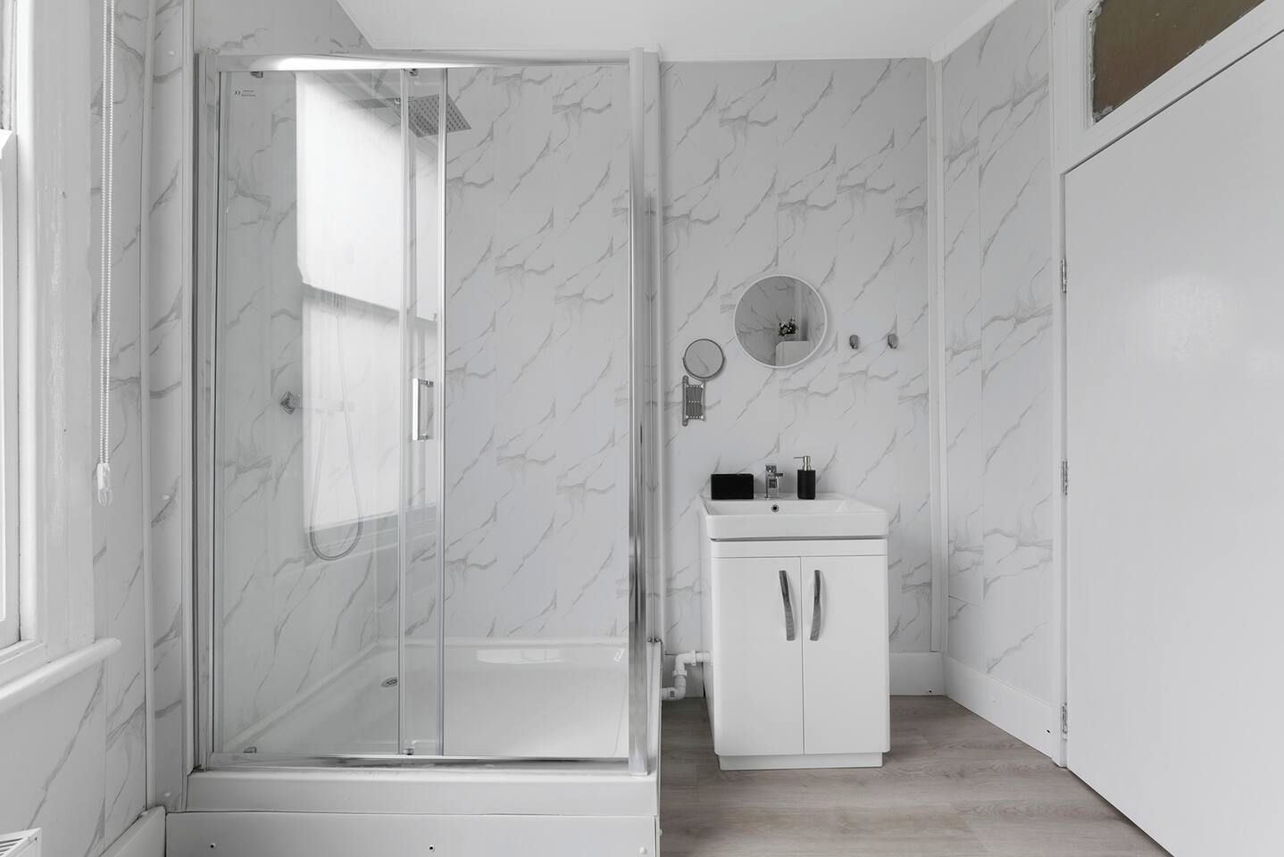 Een moderne badkamer met een douche met glazen wand, een wit wastafelmeubel met spiegel en wanden met een marmerlook.
