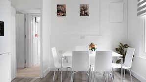 Ein moderner Essbereich mit einem weißen Tisch und Stühlen, einer Blumenvase und zwei Bildern an der Wand.