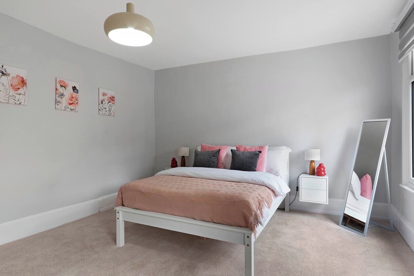 A bedroom with a bed, bedside tables, a mirror, and wall art.