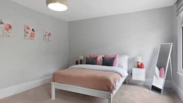 A bedroom with a bed, bedside tables, a mirror, and wall art.