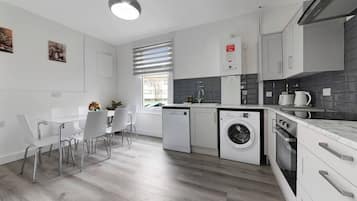 Een moderne keuken met witte kasten, een ingebouwde wasmachine en een eethoek met witte stoelen.
