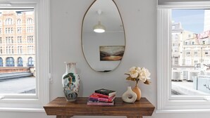 A wooden table with a vase, books, and a mirror against a wall with a view of buildings. - Shepherdess Place N1 🚇 Old Street 🚇 Angel (London)