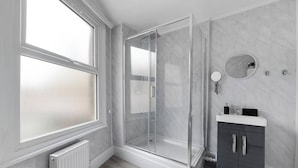 Ein modernes Badezimmer mit Duschkabine aus Glas, einem weißen Waschtisch und einer Marmor-Wand.